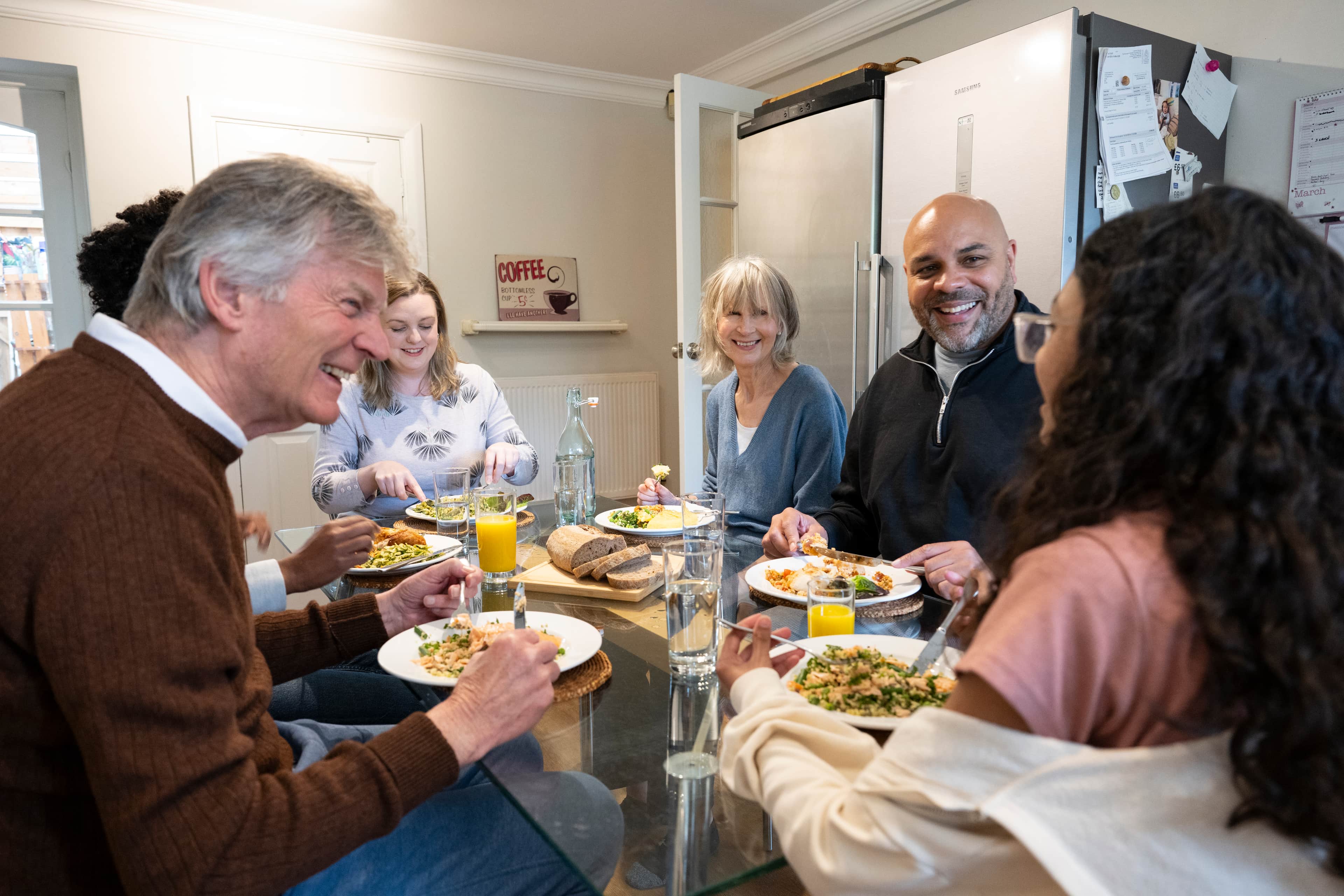 Group of adults smiling while eating a meal together at a table.