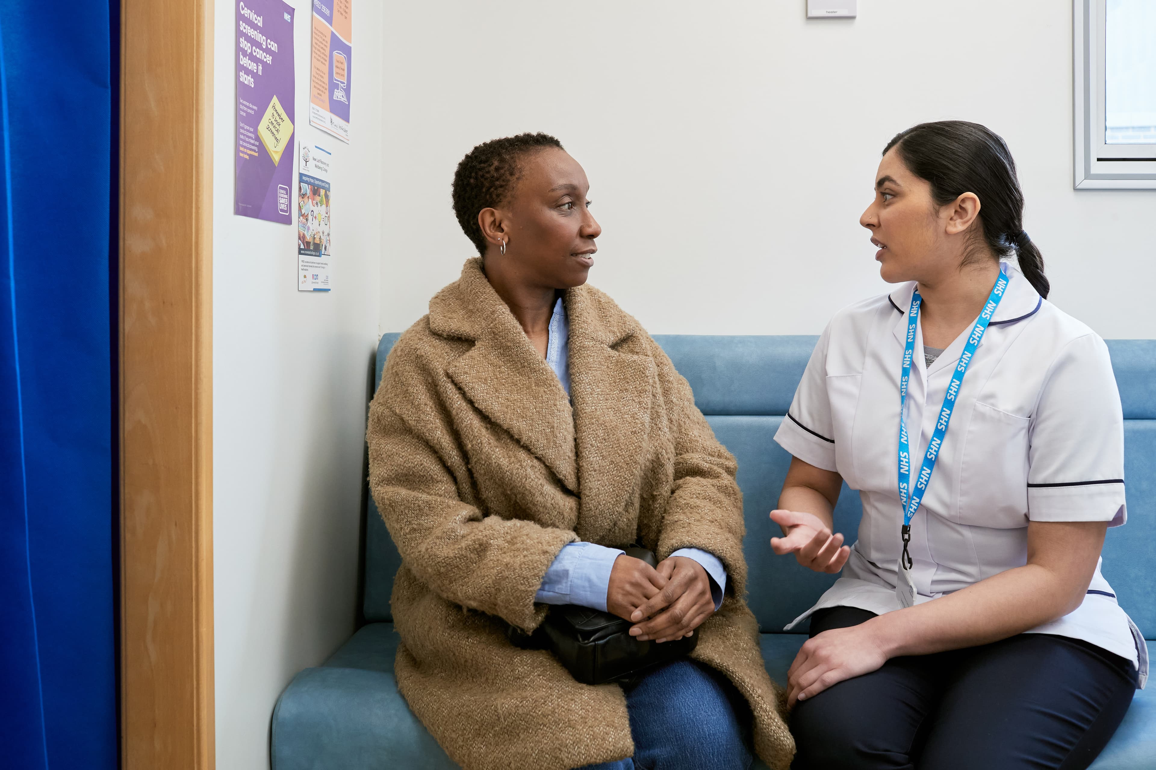 This photo shows a mammographer with a patient, wearing a hospital gown, before a mammogram.