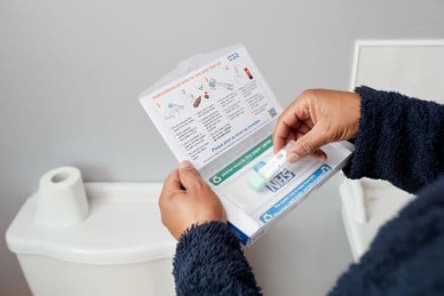 Photo showing a man in a bathroom opening a bowel cancer screening test kit from NHS England.